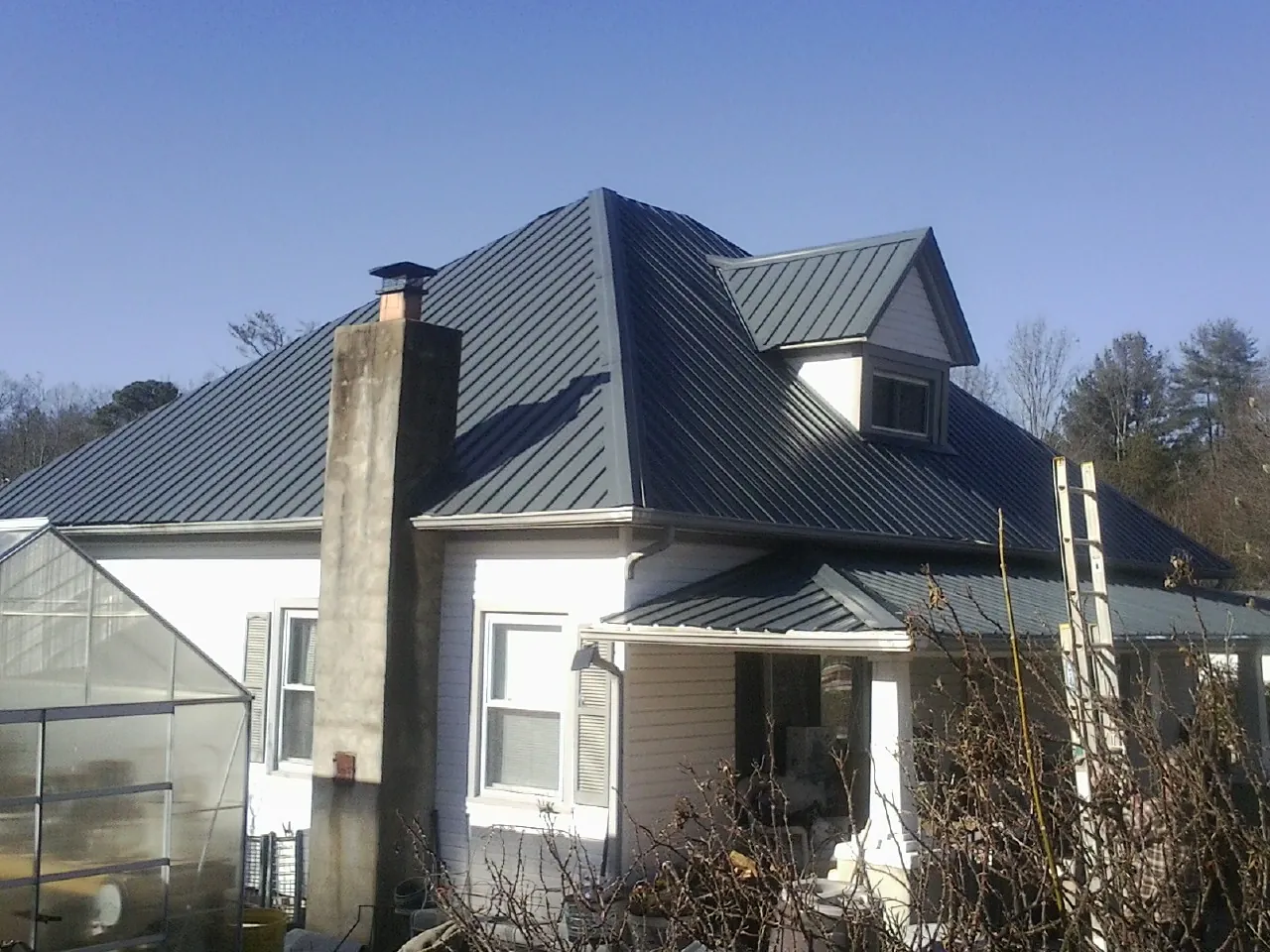 Dark blue standing seam metal roof on a white farmhouse with dormer — Slate & Tile Roof Repair by Roofing Brothers in Plain