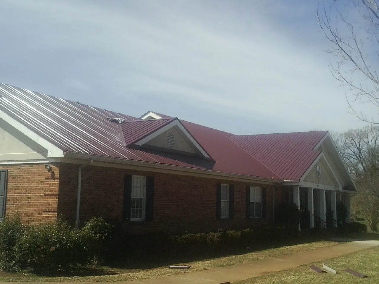 Red metal roof with gabled entries on a long brick building, from a Hail Damage Roof Repair job in Plain