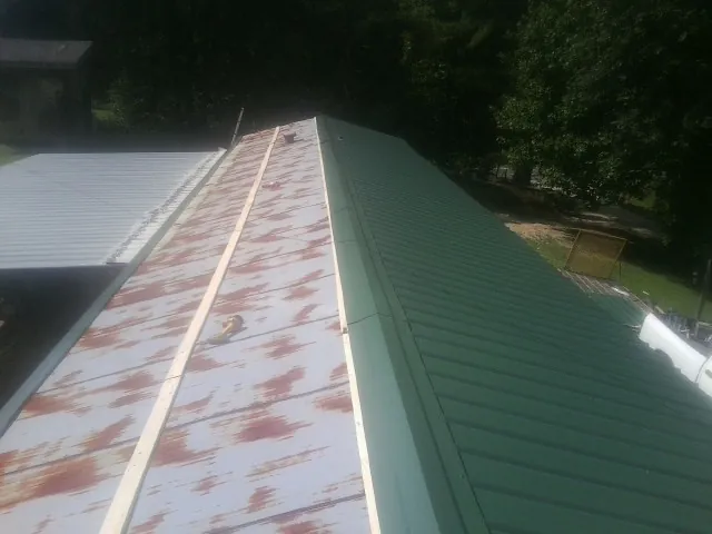 Old rusted panels beside newly installed green metal roofing — Wind Damage Roof Repair by Roofing Brothers in Plain