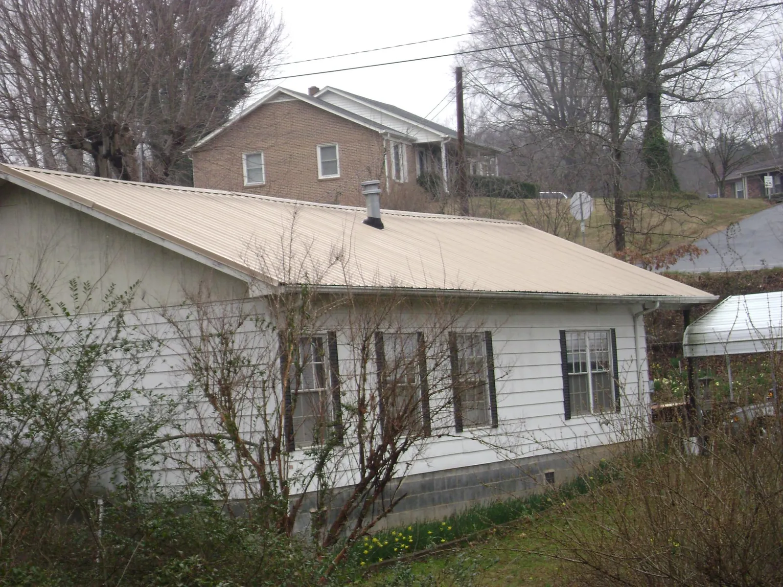 Tan metal roof on a white sided house set into a hillside — Commercial Roofing by Roofing Brothers in Plain